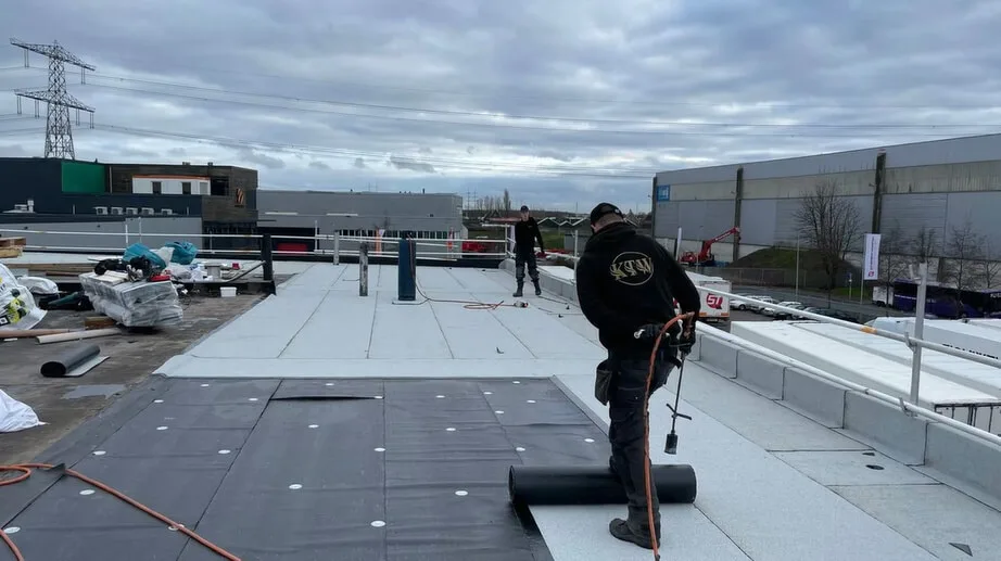 Twee KTW dakdekkers leggen bitumen dakbedekking op een groot plat bedrijfsdak